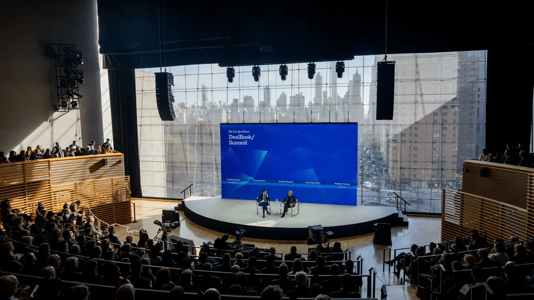 The Times Center auditorium during the DealBook Summit, with a full audience and the stage framed by tall windows